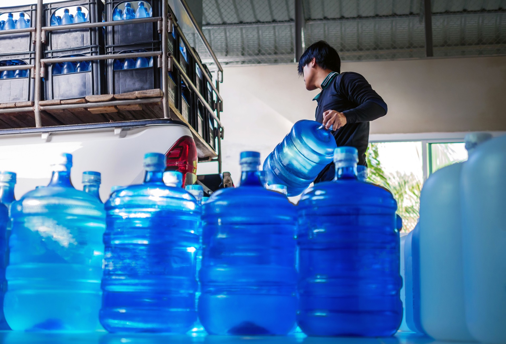 Workers lift drinking water 
clear and clean in blue plastic gallon into the back of a transport truck purified drinking water inside the production line to prepare for sale. Water drink factory, small business