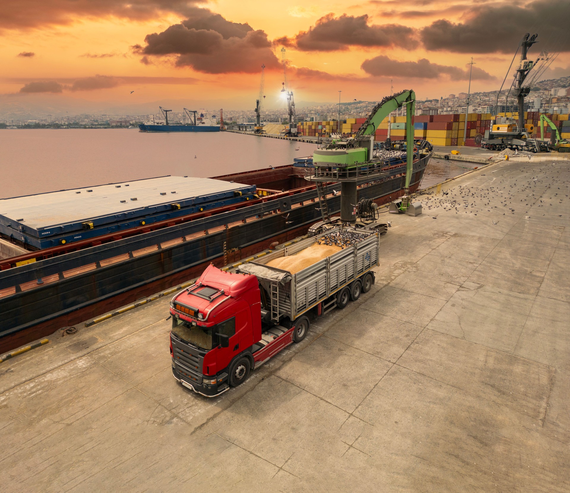 Loading operations with a portal crane in a warehouse in the port. Grain transshipment from cargo ship to truck holds